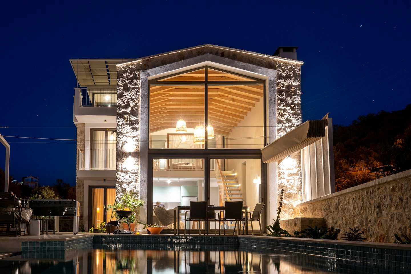Villa moderna di notte con finestre illuminate e piscina.