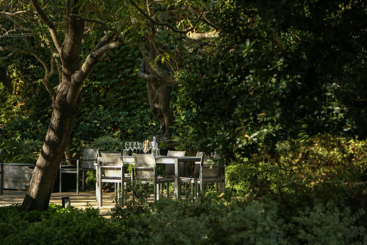 Tavolo da pranzo all'aperto apparecchiato con bicchieri e bottiglia di vino in un giardino.