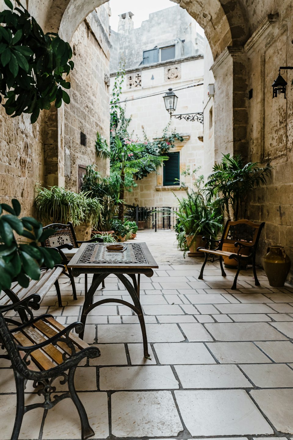 Cortile in pietra con tavolo a mosaico e piante in vaso.