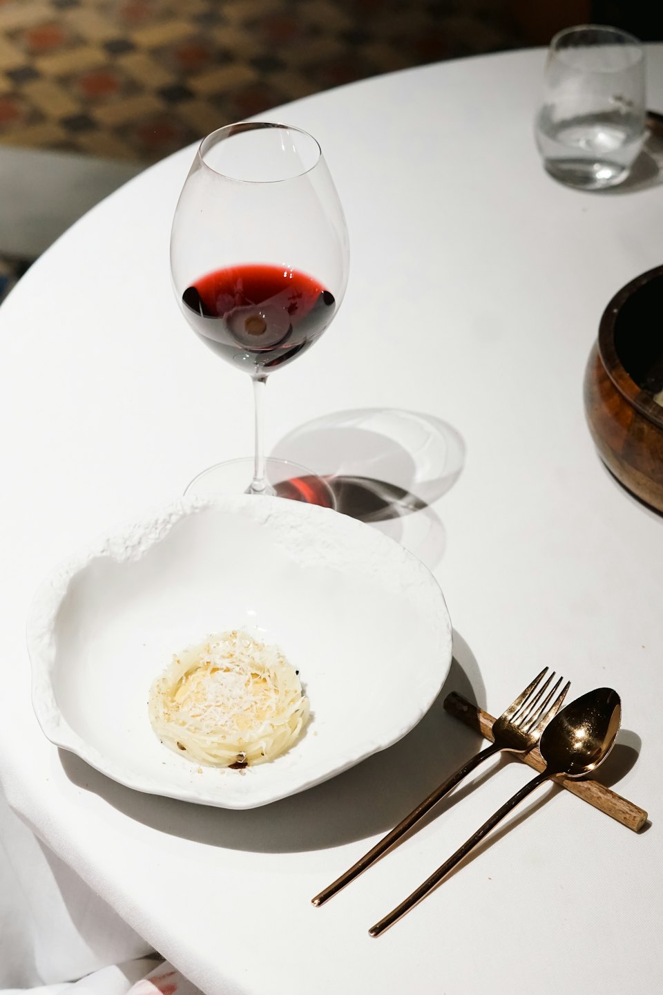 Un piatto bianco con cibo, vino rosso e posate di bronzo su una tovaglia.
